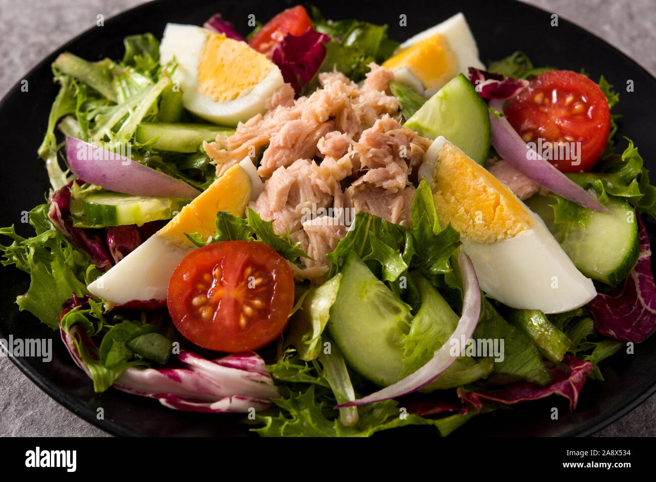 Salat mit Thunfisch, Ei und Gemüse auf schwarz und grau hinterlegt. Nahaufnahme Stockfoto