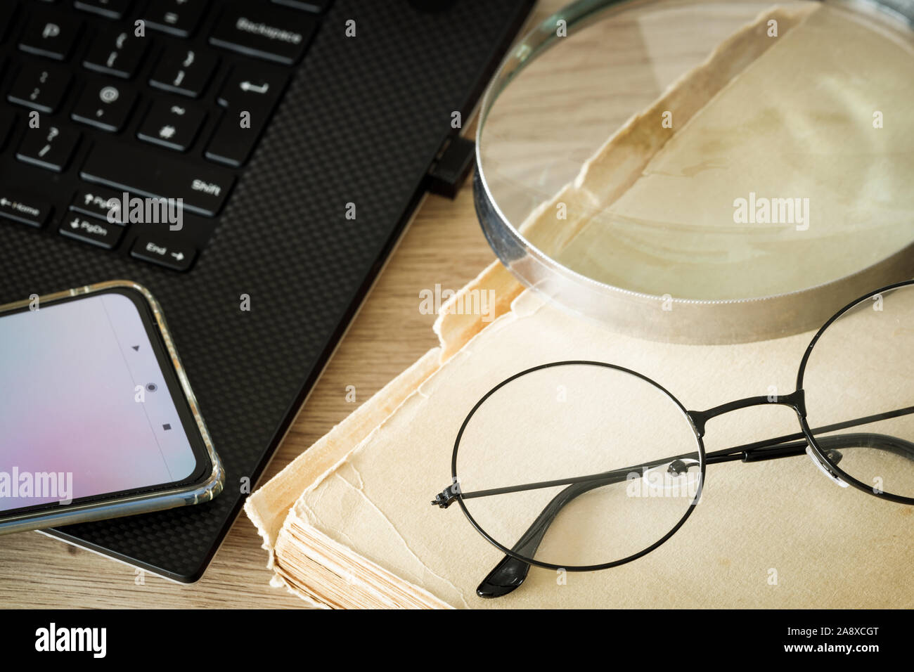 Ein Buch, altmodische Brille, eine Lupe und Laptop mit einem Smartphone. Konzept, einer Kombination aus modernen Technologien und der traditionellen Methoden der r Stockfoto