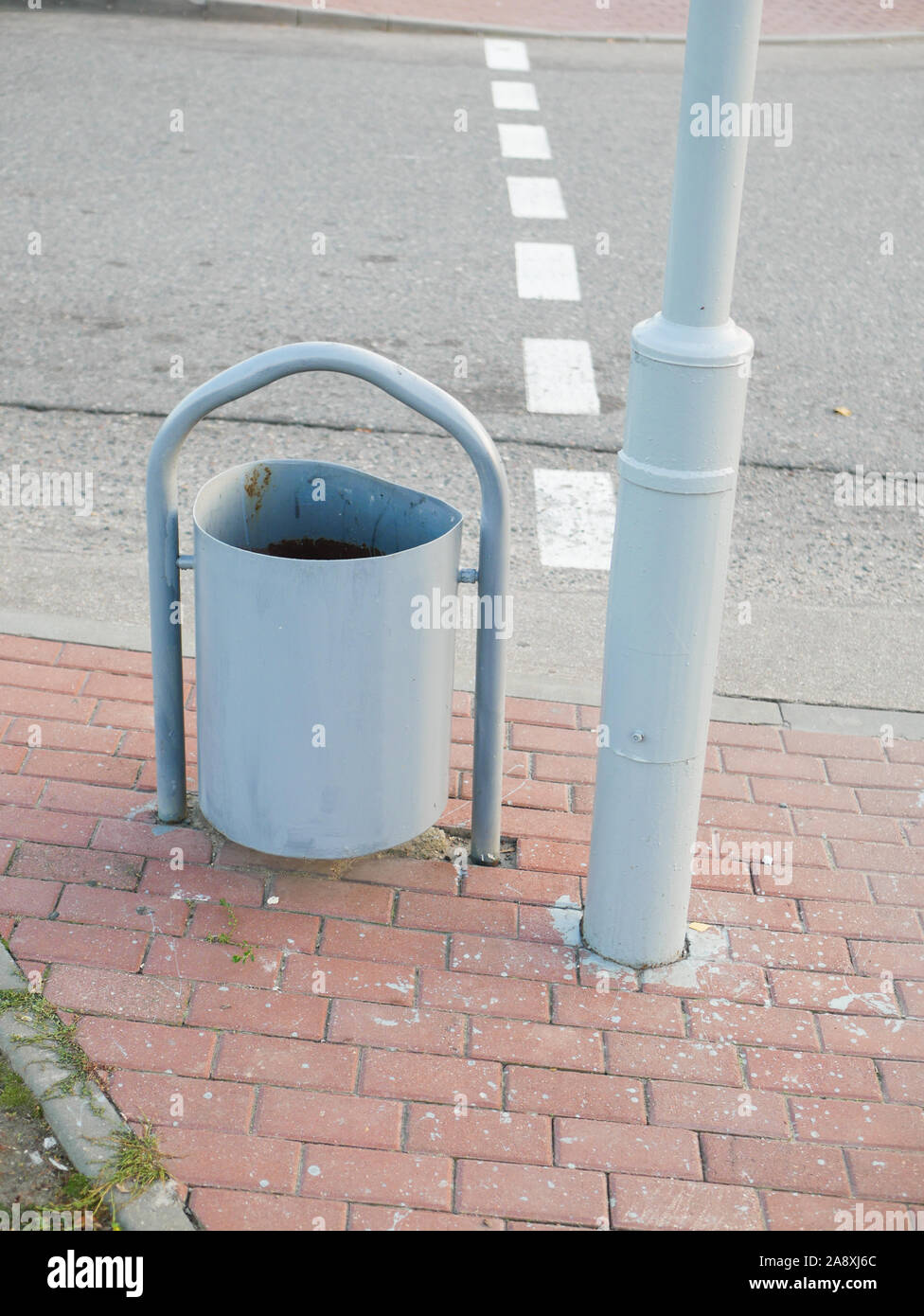 Metall Urne in der Nähe der Straße. Ein Metall Mülleimer steht in der Nähe der A-Säule auf dem Bürgersteig. Schmieden von Mülltonnen steht in der Nähe eine Bank, auf dem Bürgersteig Stockfoto