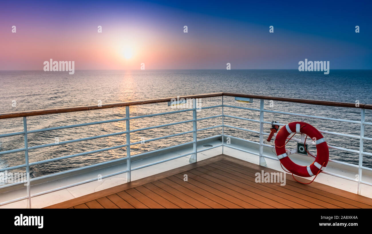Landschaftlich schöne Aussicht auf den Sonnenuntergang vom Deck eines Kreuzfahrtschiffes mit Sicherheitsgeländer im Vordergrund. Stockfoto