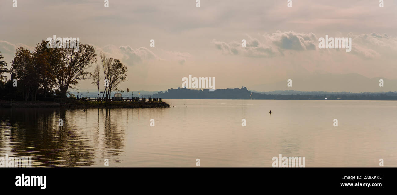 Misty Blick auf den Trasimenischen See in Umbrien mit Isola Maggiore (größere Insel) und Castiglione del Lago Altstadt und Wände im Hintergrund Stockfoto