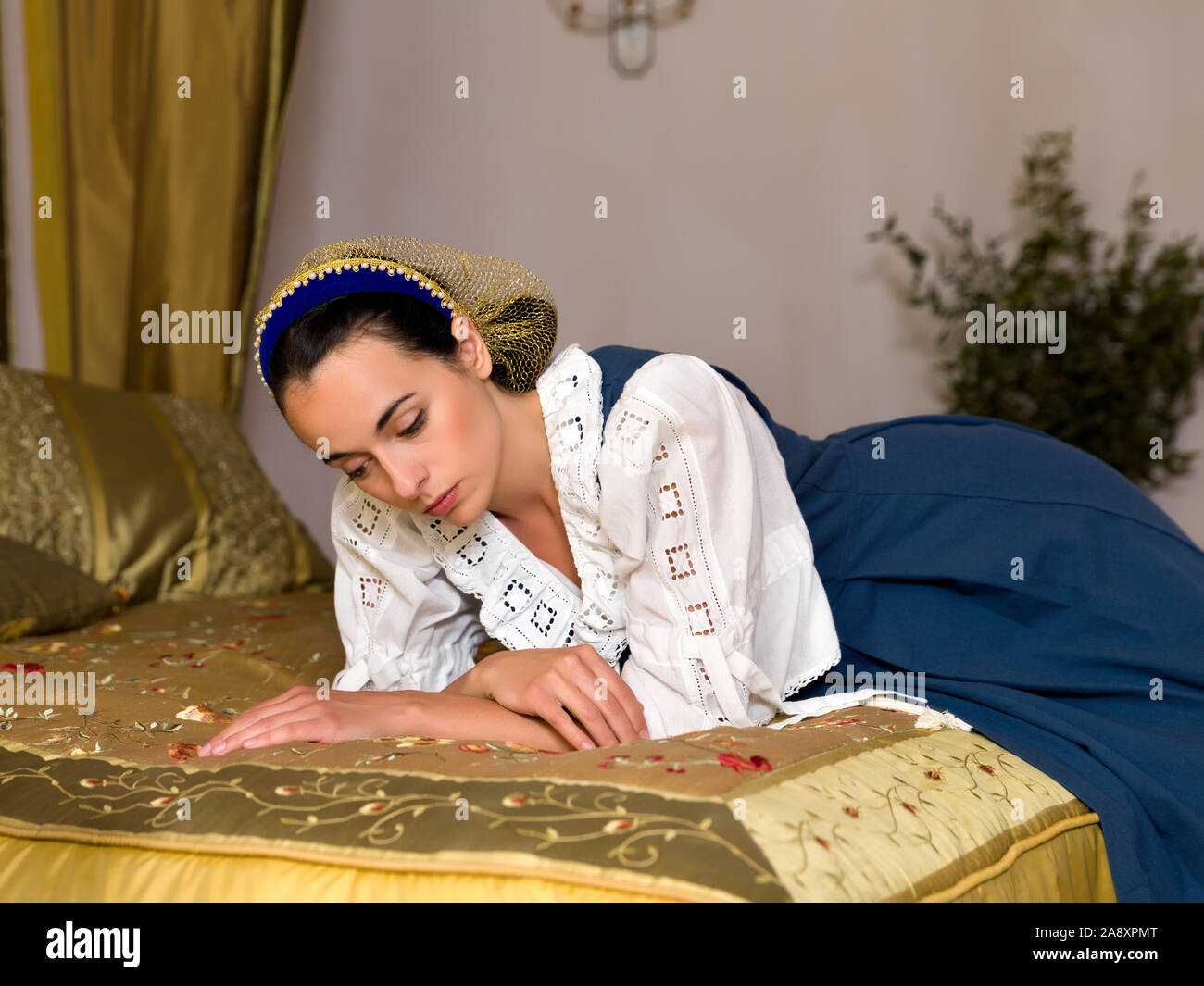 Dutch Master Stil Porträt einer schönen jungen Frau in authentische Renaissance Kostüm liegen auf einem luxuriösen antiken Himmelbett in einem goldenen Schlafzimmer eines Stockfoto
