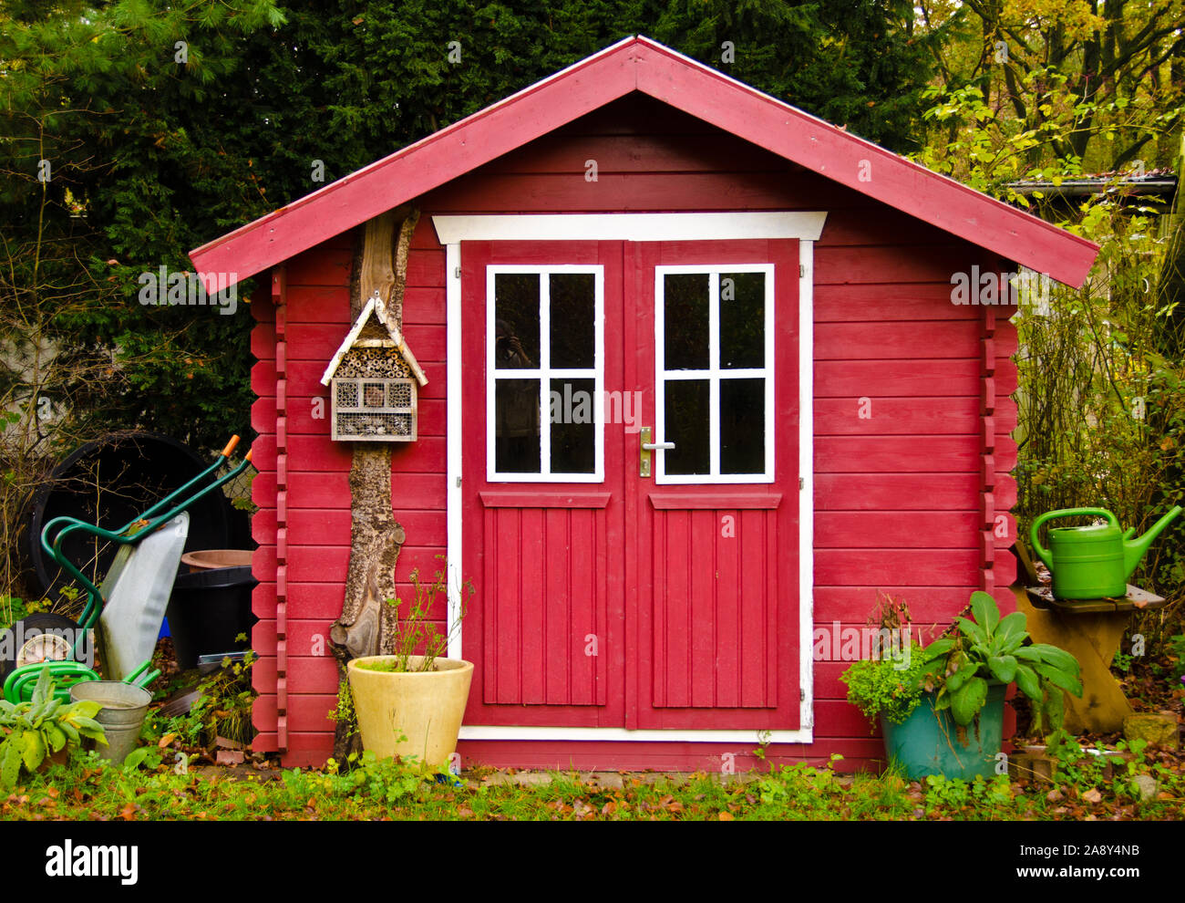 Ein helles Rot kleine Schuppen Gartenhaus, mit einigen Garten Tools rund um die IT Stockfoto