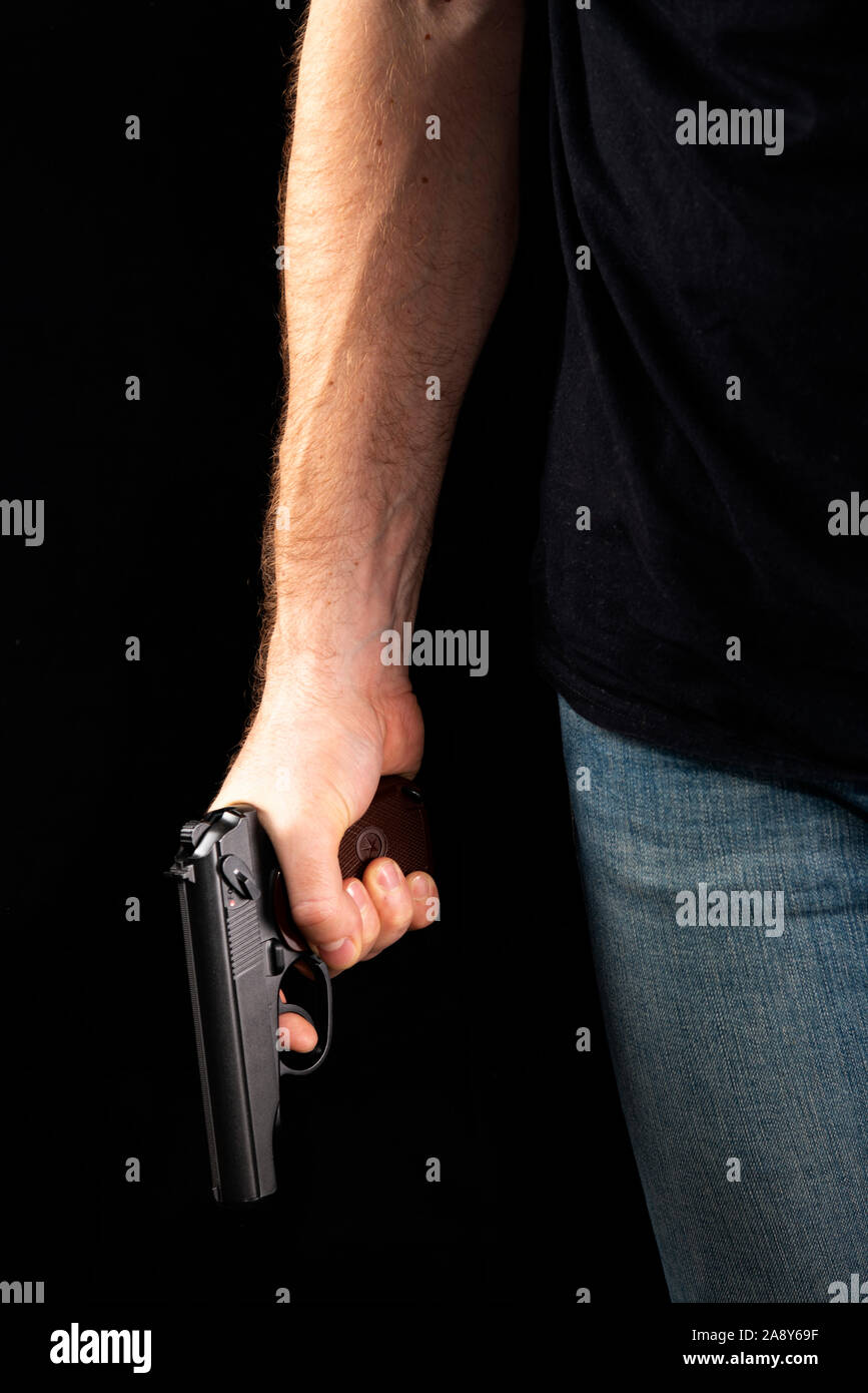 Ein Mann mit einer Waffe in der Hand auf einem schwarzen Hintergrund. Killer mit einer Pistole Stockfoto
