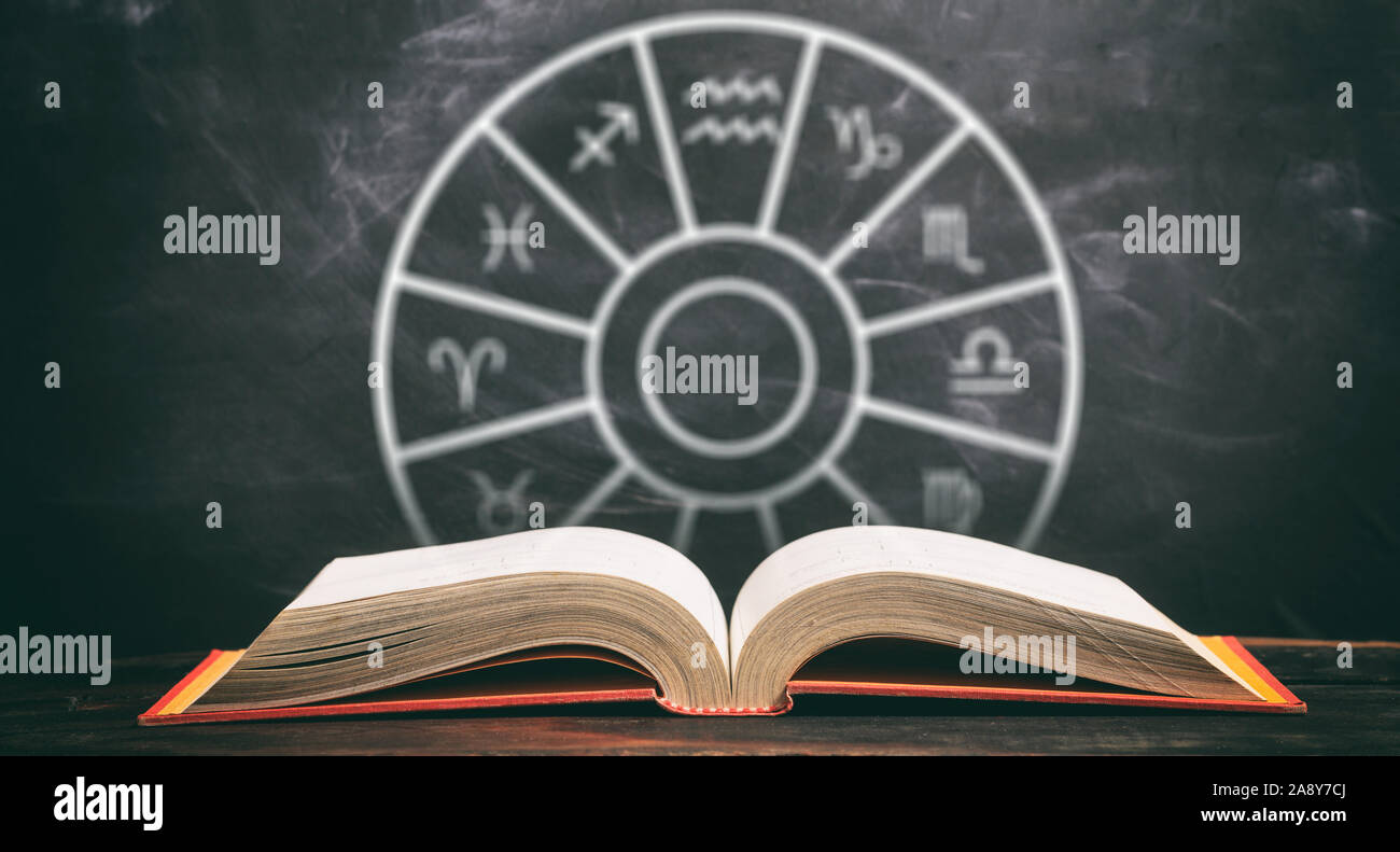 Astrologie und Horoskope Konzept. Buch und astrologischen Tierkreiszeichen Rad, schwarzer Hintergrund öffnen. Stockfoto