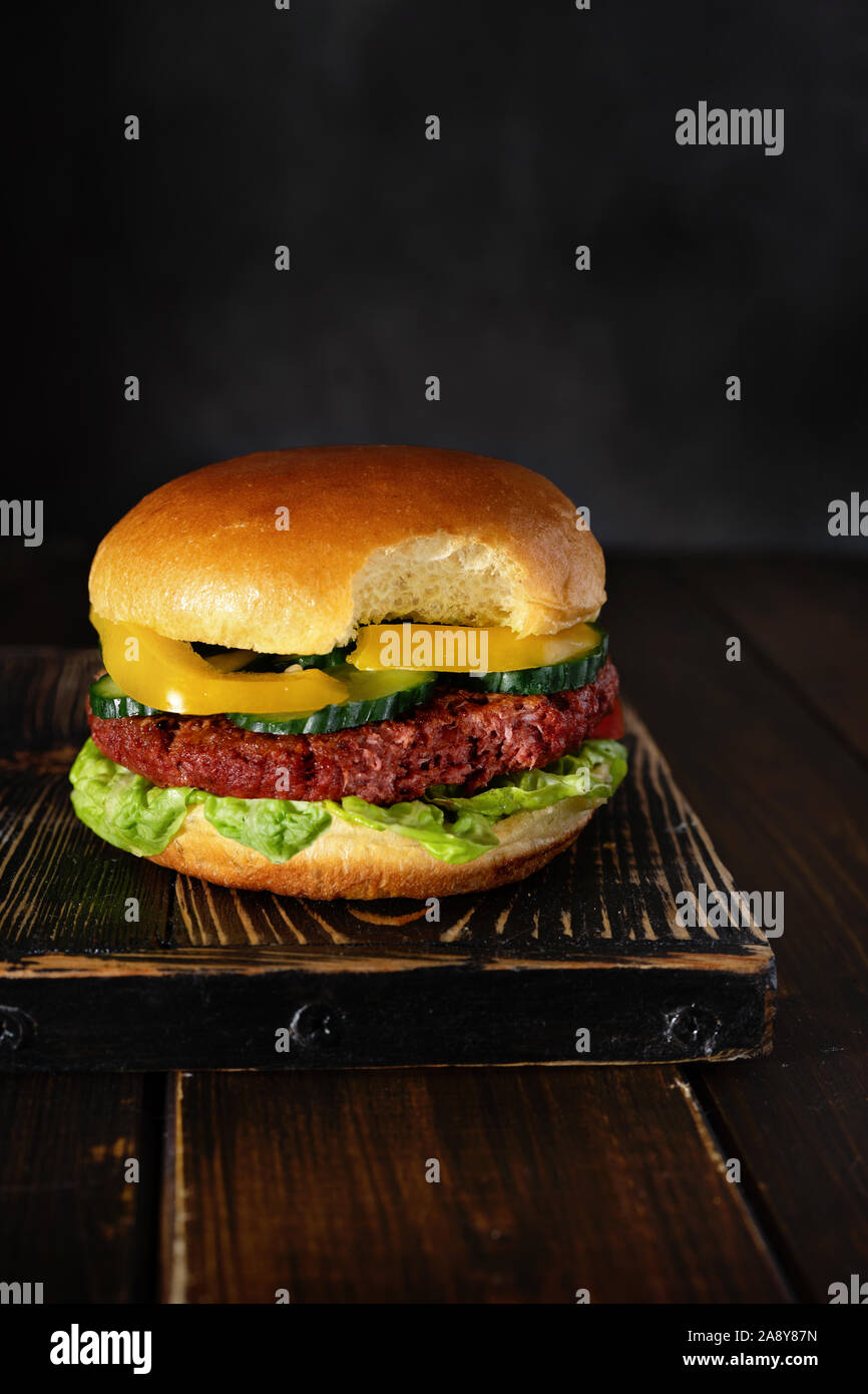 Gebissen vegetarische Burger auf Holzbrett auf dunklem Hintergrund Stockfoto