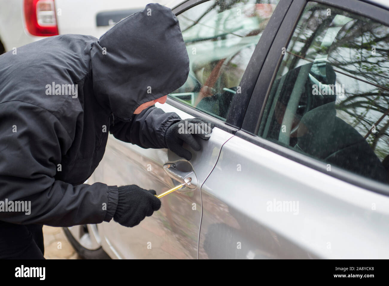 Ein Räuber in Schwarz holding Brecheisens ein Fahrer in einem Auto gekleidet. Auto Dieb, Autodiebstahl Konzept. Stockfoto