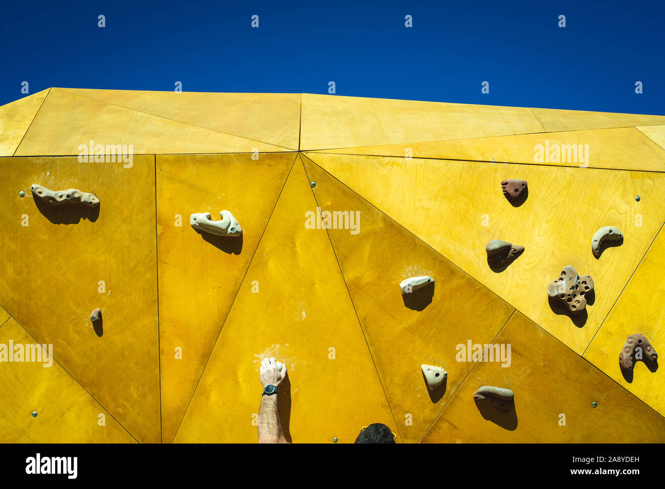 Junger Mann greift, um zu versuchen, Klettern an einer Kletterwand im Freien in einem Park in Valencia. Stockfoto