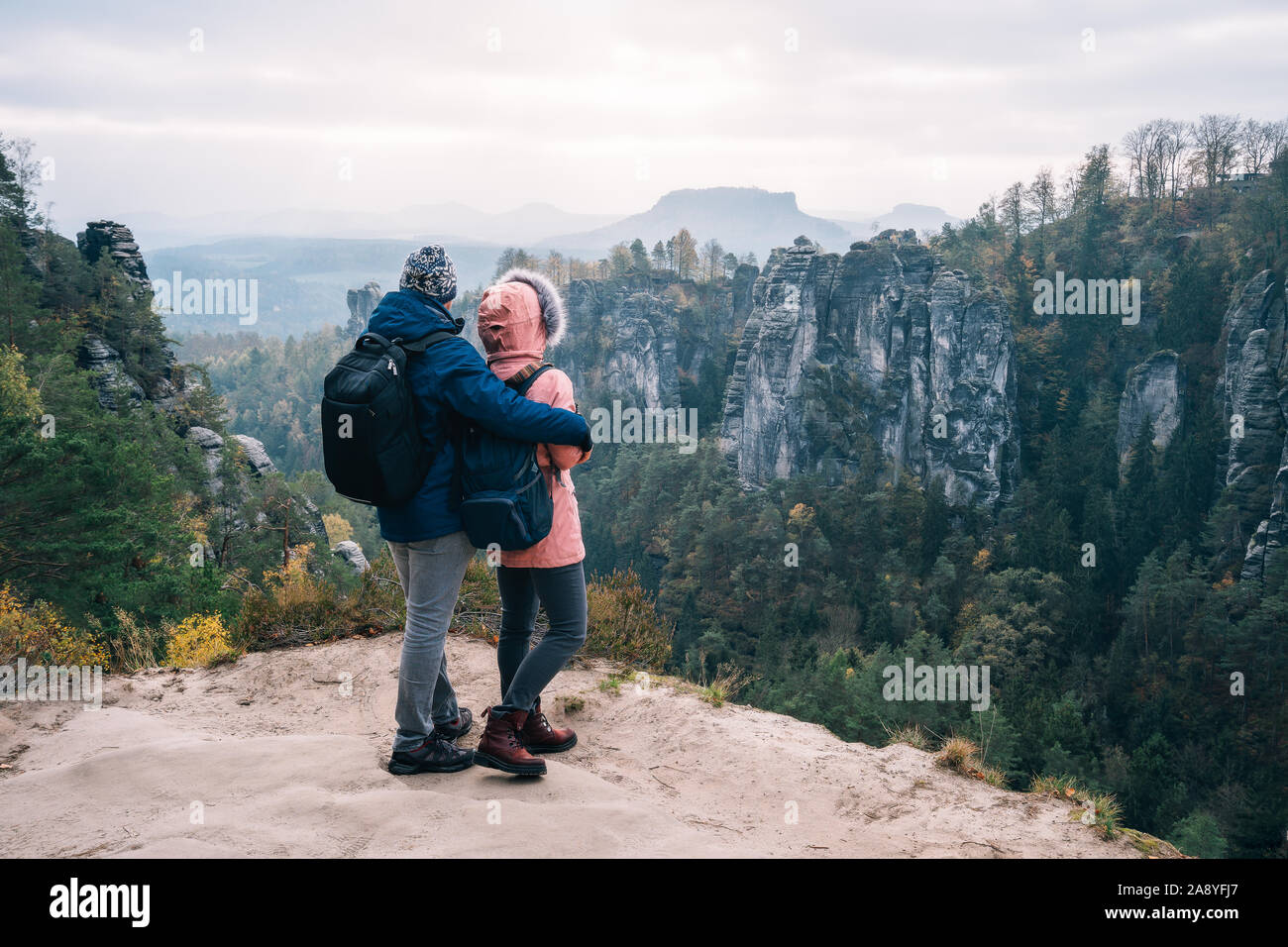 Junges Paar in Outdoor Bekleidung mit Rucksäcken auf Plateau mit Blick auf den Bergrücken und wilden Wald im Tal am Wanderweg Stockfoto