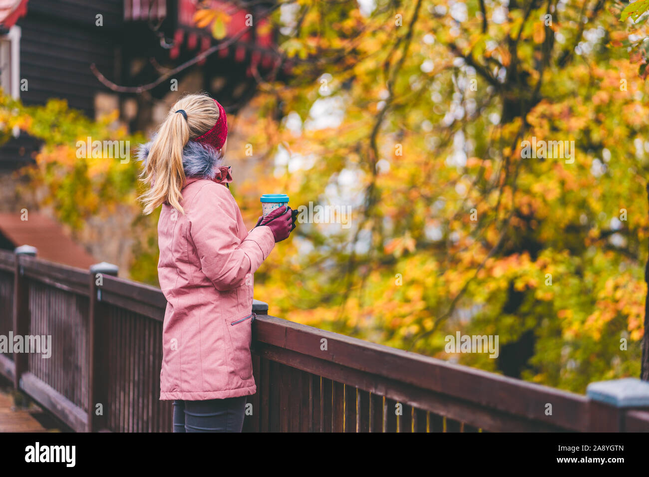 Nach blonde Frau hält eine Tasse Kräutertee T-Stück in die Hände auf Holzbrücke mit schönen goldenen Herbst Blätter im Hintergrund Stockfoto