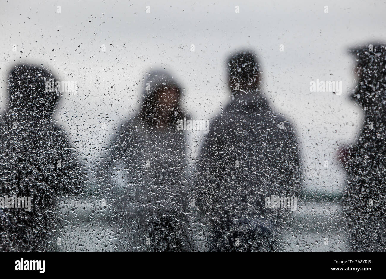 Menschen, die auf der Außenseite Deck auf einem Washington State Ferry im Regen durch ein Fenster mit Regentropfen fallen gesehen, den Schwerpunkt auf die Regentropfen. Stockfoto