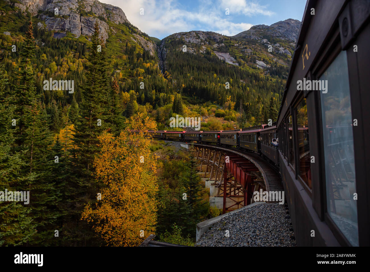 Skagway, Alaska, Vereinigte Staaten - 24 September 2019: Alte historische Eisenbahn Zug fährt über eine Holzbrücke bis White Pass mit Touristen während einer cl Stockfoto