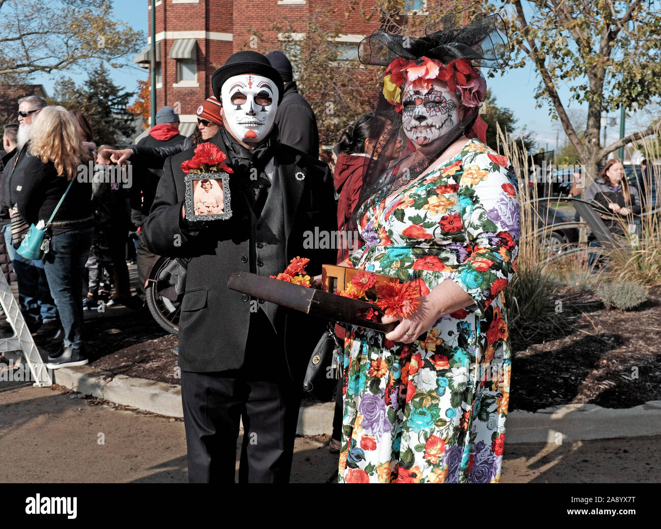 Ein paar in bunten skull Make up und Maske feiern Dia de los Muertos in Cleveland, Ohio, USA halten momentos von Lieben, die weitergegeben. Stockfoto