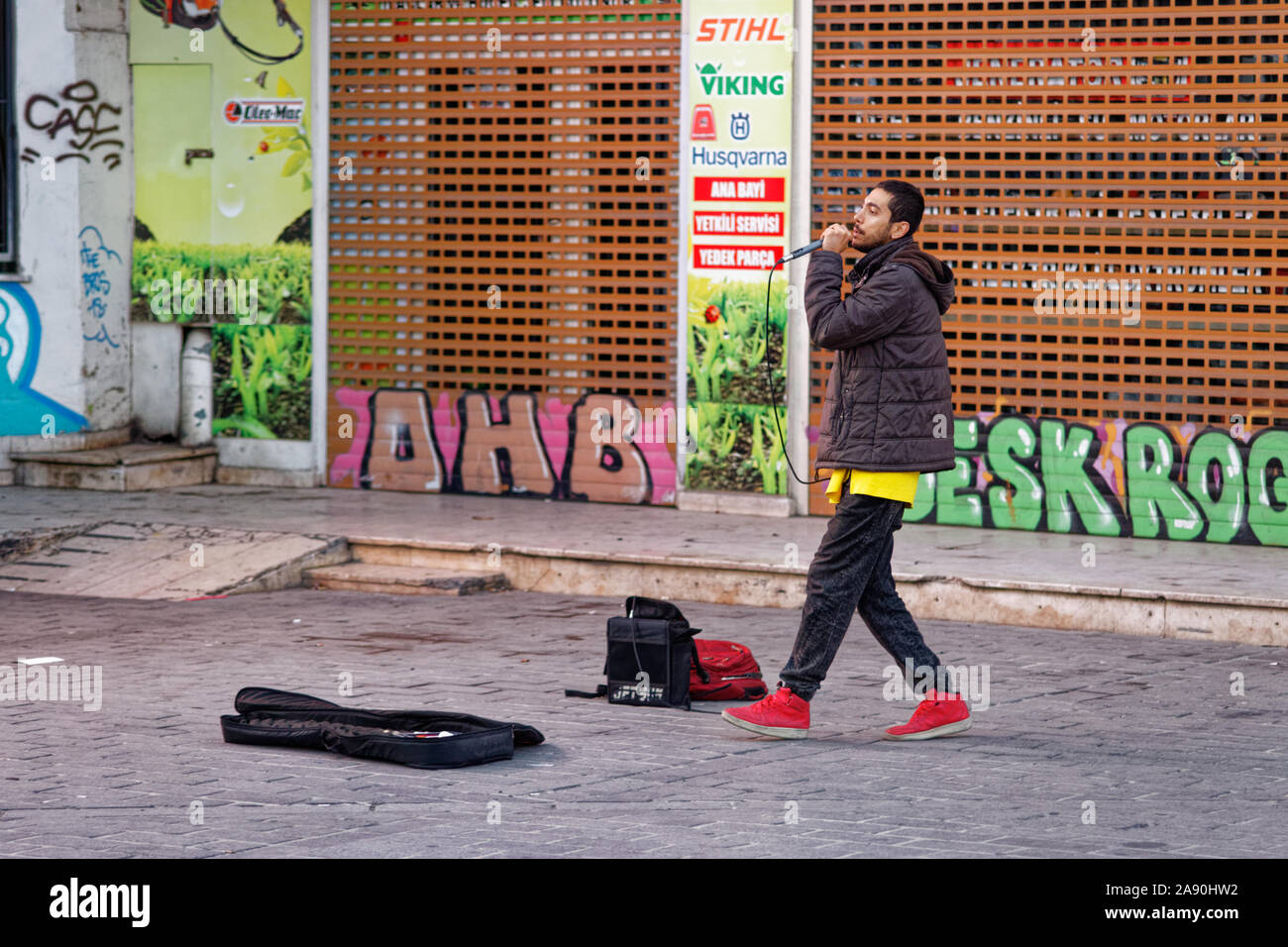 Männliche Straßenmusiker singen Rap Song in Karaköy/Istanbul während der Abendstunden. Eine E-Gitarre und tragbare Lautsprecher Verstärker weiter hinter ihm. Stockfoto