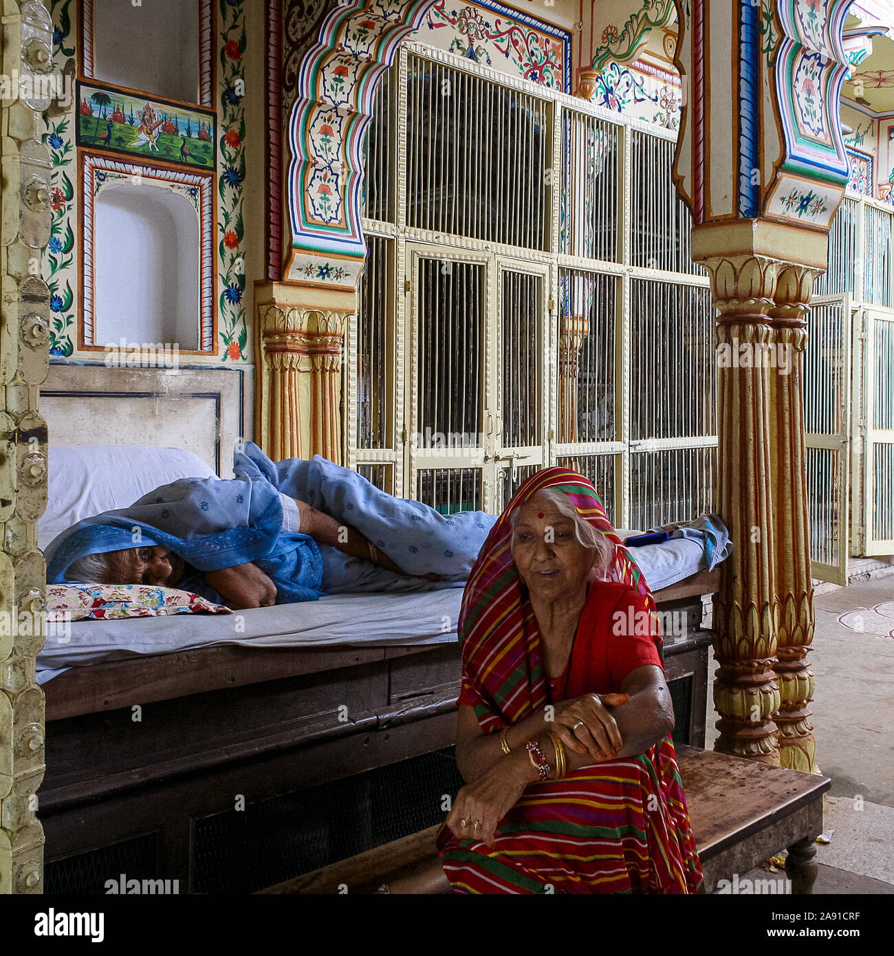 Pushkar, Rajasthan, Indien: Eine ältere Indianerin schläft auf dem Bett, während eine andere Frau neben ihr sitzt. Stockfoto