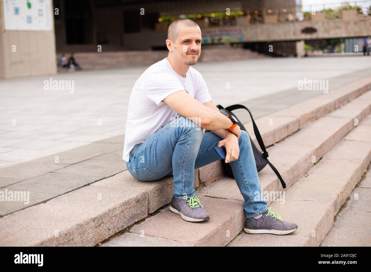 Mann sitzt auf der Treppe im Park mit Rucksack hinter ihm Stockfoto