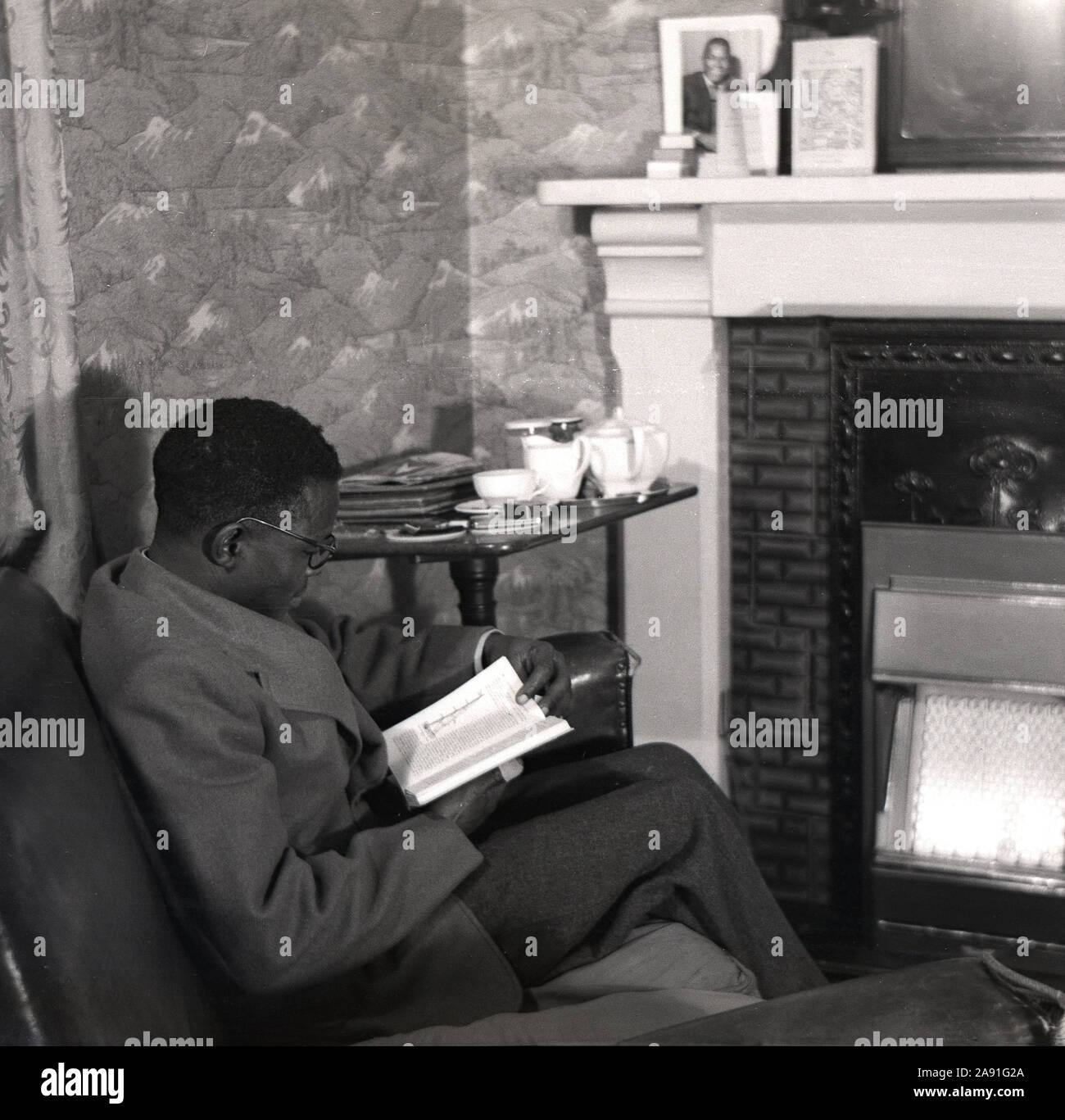 1950, historische, eine ausländische ausländischen Studenten aus einem afrikanischen Land in seiner bedsit studieren, England, Großbritannien sitzen. Stockfoto