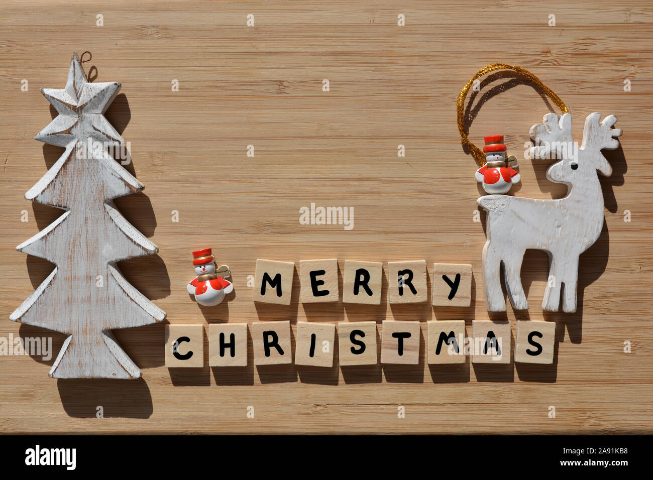 Frohe Weihnachten in 3d Holz- Buchstaben des Alphabets mit einem hölzernen Weihnachtsbaum, Rentiere und Santa Schneemänner Dekorationen auf einem bambus holz Hintergrund mit Co Stockfoto