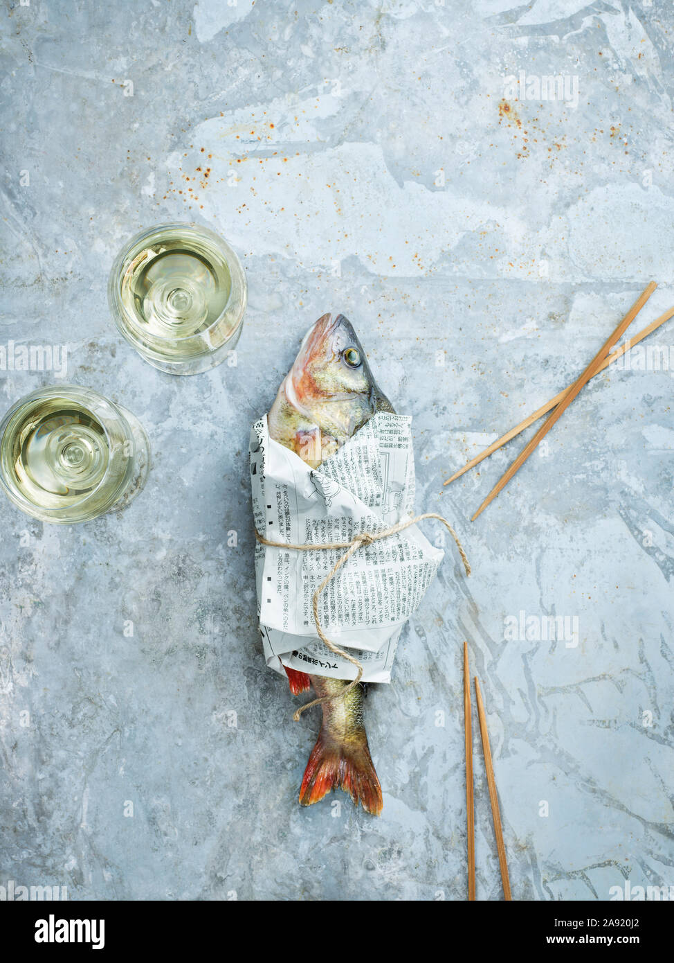 Weingläser und rohen Fisch in Zeitungspapier gewickelt Stockfoto