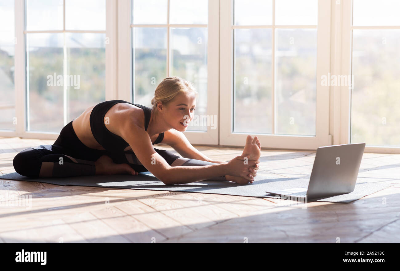 Flexible girl Yoga zu Hause, beim Laptop Bildschirm schaut Stockfoto