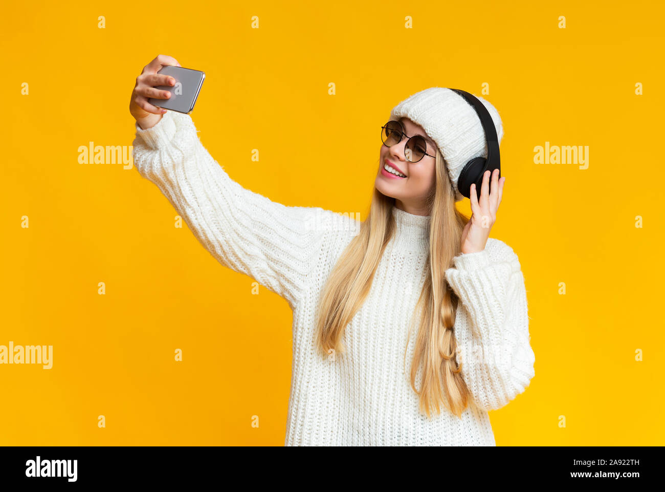 Fröhliche blonde Mädchen im Winter Hut und Headset unter selfie Stockfoto