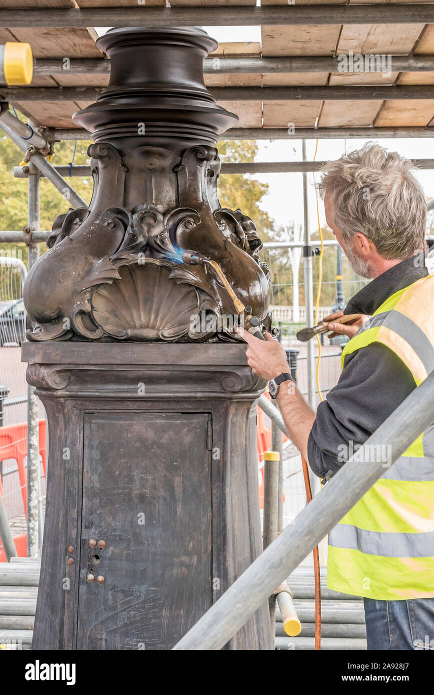 London, Großbritannien. 6. November 2019. Wesentliche Arbeit im Naturschutz findet an der Queen Victoria Memorial direkt vor dem Buckingham Palace entfernt. Spezialisierte Teams arbeiten mit einem bestimmten Gefühl der Dringlichkeit und einen akuten Bewusstsein der königlichen Frist gewährleistet die vollständige Entfernung/Demontage der unansehnlichen Gerüst vor der jährlichen Erinnerung Sonntag Parade am 10. November dieses Jahres gehalten werden. Eine isolierte Erhaltung Experte arbeiten alleine mit einem Brenner, blowlamp in der einen Hand und Pinsel für Wachs in die andere. Quelle: Lee Hudson Stockfoto