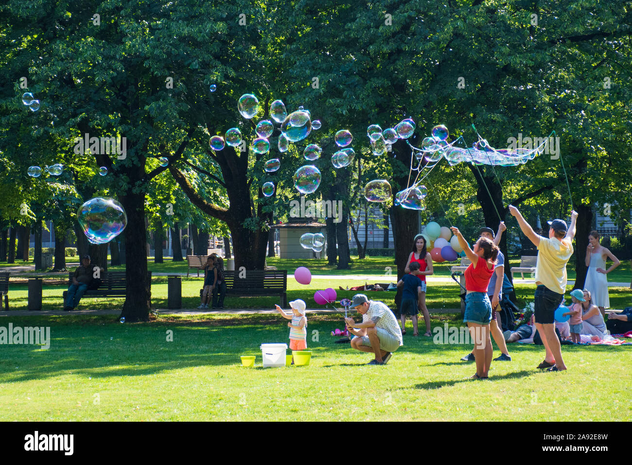 Kinder spielen im Freien in einem Park mit Ihren Eltern an einem sonnigen Tag, mit Seifenblasen Stockfoto