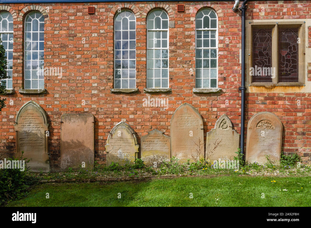 Alte Grabsteine aufgereiht gegen das Äußere des Baptistischen Kapelle im Dorf von Earls Barton, Northamptonshire, Großbritannien Stockfoto