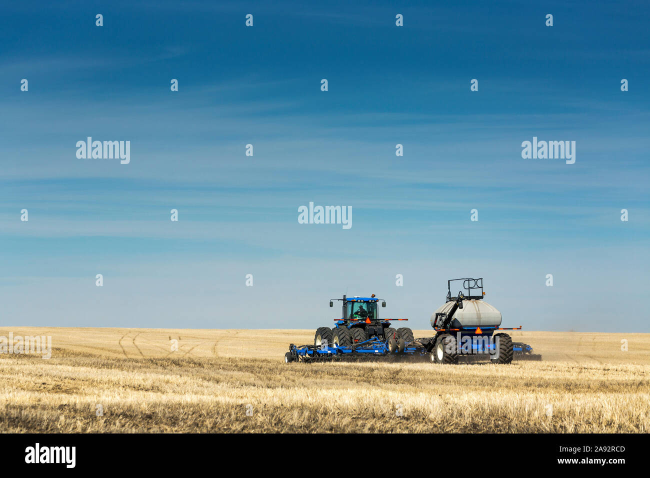 Traktor mit Luftsämaschine im Feld mit blauem Himmel und trüben Wolken, in der Nähe von Beiseker; Alberta, Kanada Stockfoto