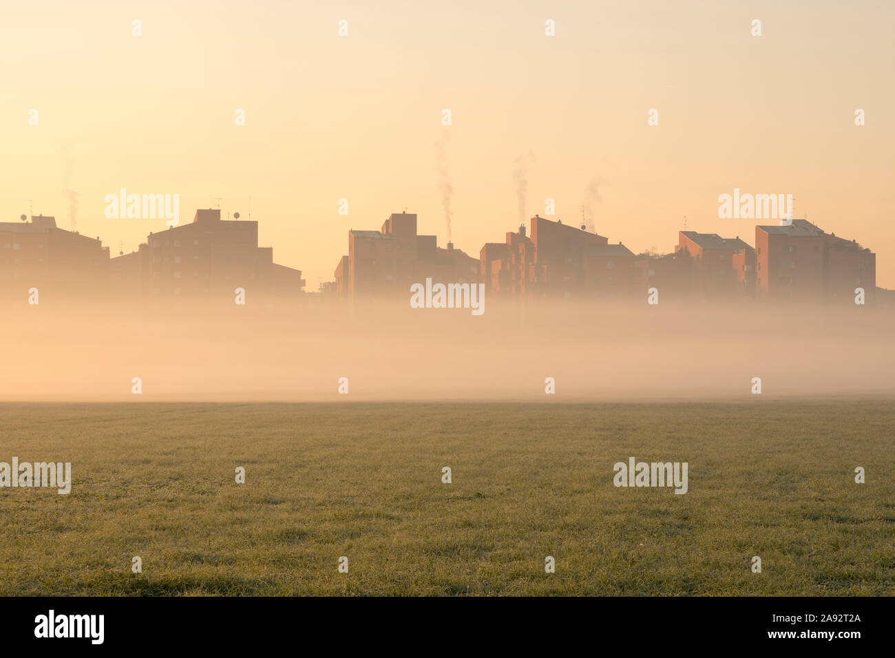 Stadtbild bei Sonnenaufgang. Häuser am Rande der Stadt mit Nebel im Morgengrauen im Winter. Tritt Rauch aus den Schornsteinen. Stockfoto