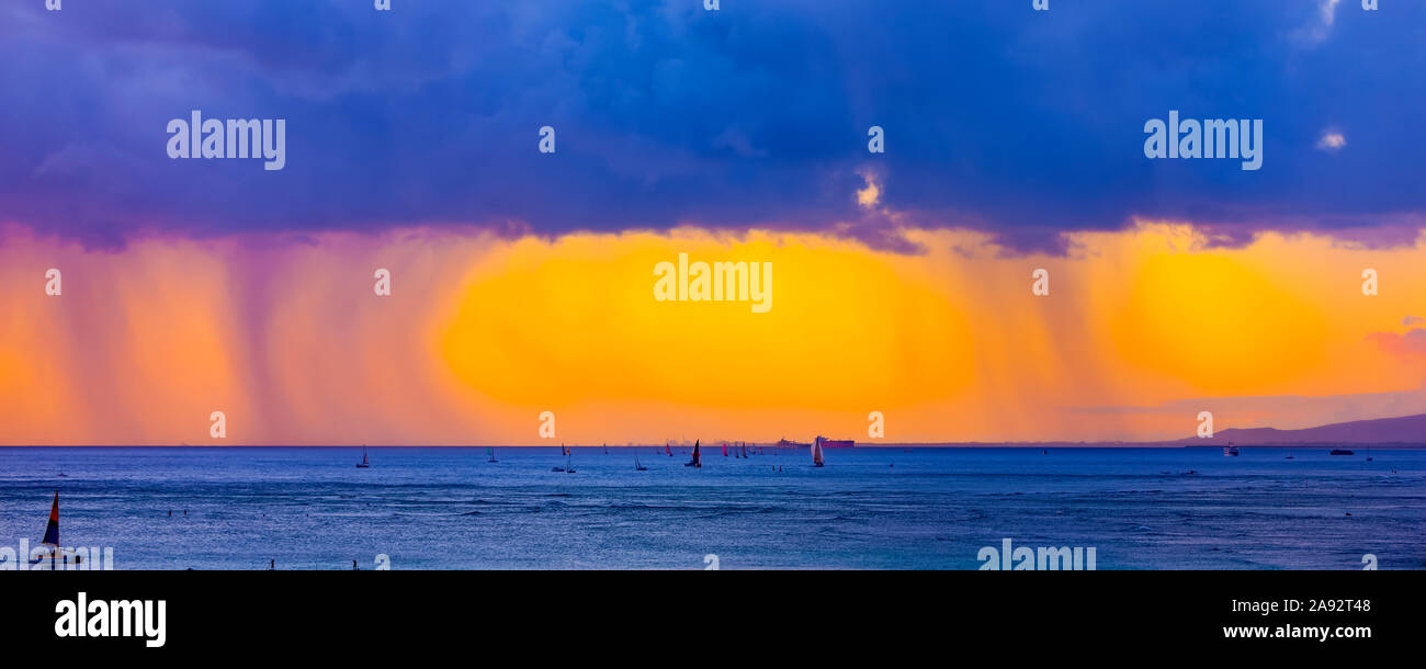 Sturmwolken mit Regen und Wolken, die ein helles Gelb leuchten Bei Sonnenuntergang vor Waikiki Beach mit einem silhouetted Segelboote in Das Wasser Stockfoto