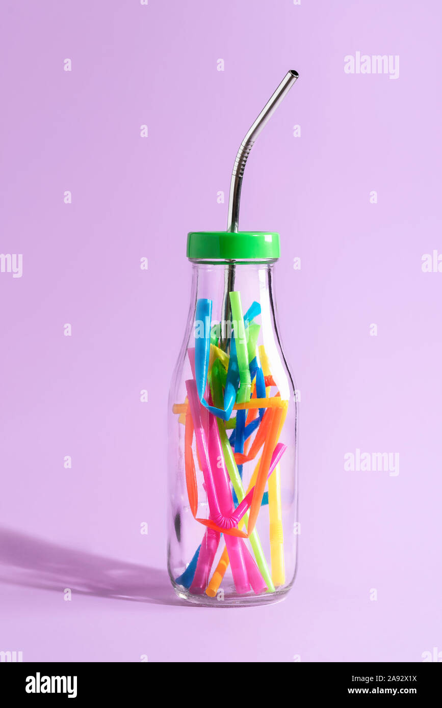 Kunststoff Verschmutzung Konzept mit einem wiederverwendbaren Metall Stroh in einer Glasflasche mit bunten Kunststoff reduzieren, auf lila Papier. Umweltfreundliche Trinkhalm. Stockfoto