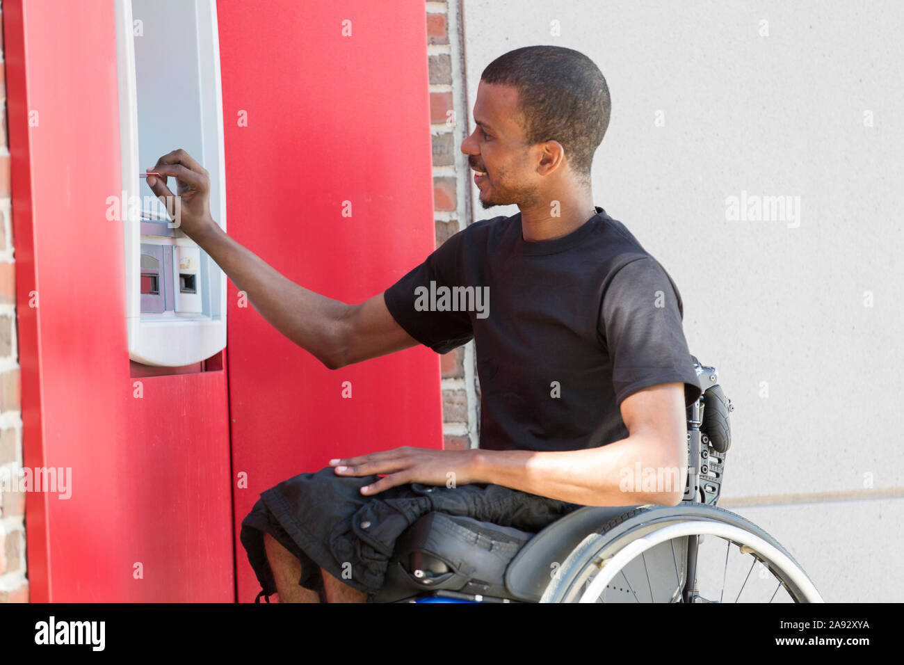 Mann, der Spinale Meningitis in einem Rollstuhl bei A hatte geldautomat Stockfoto