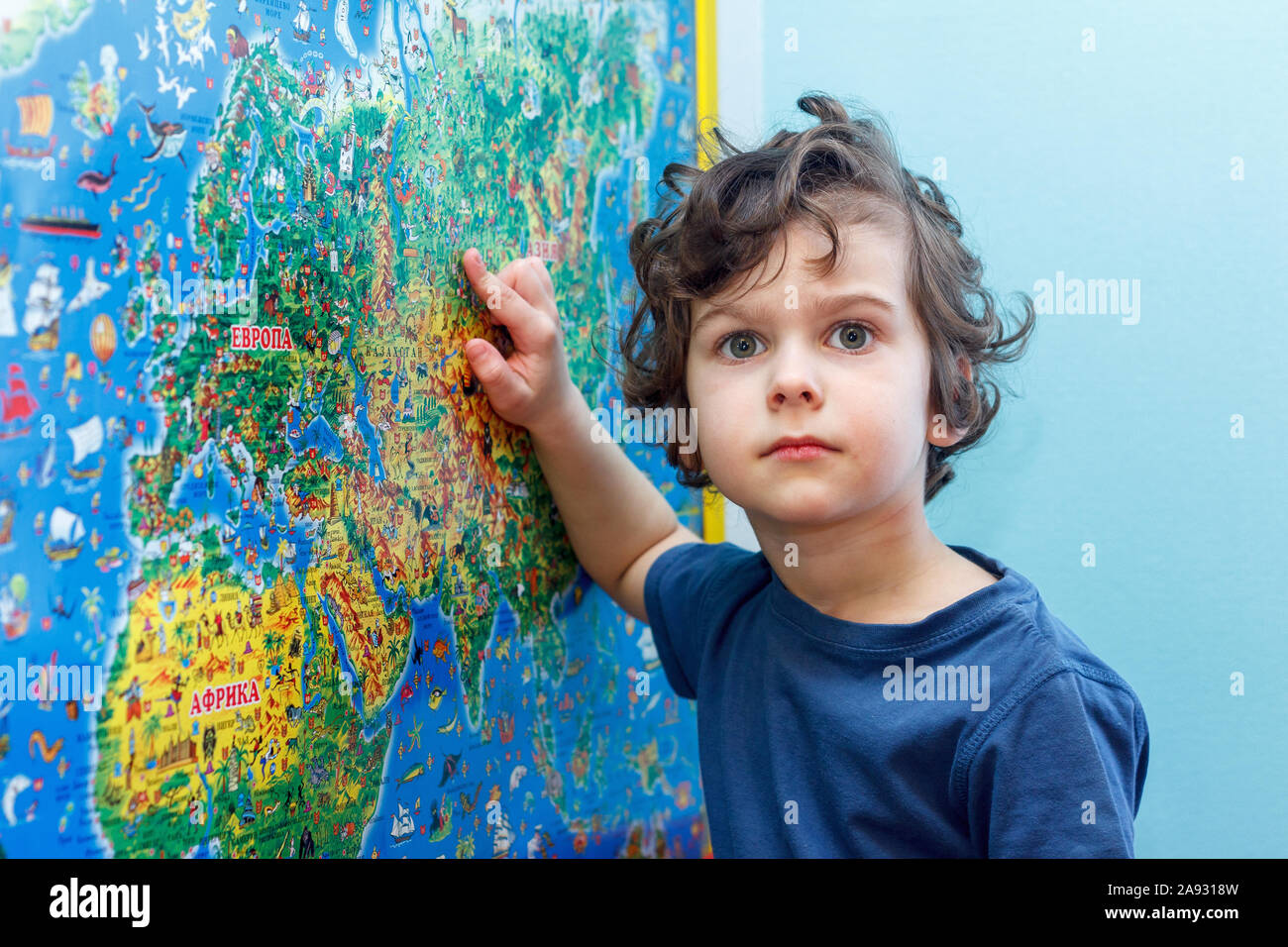 Das lockige Kind mit Interesse betrachtet die blaue Weltkarte als Europa und als Afrika. Stockfoto