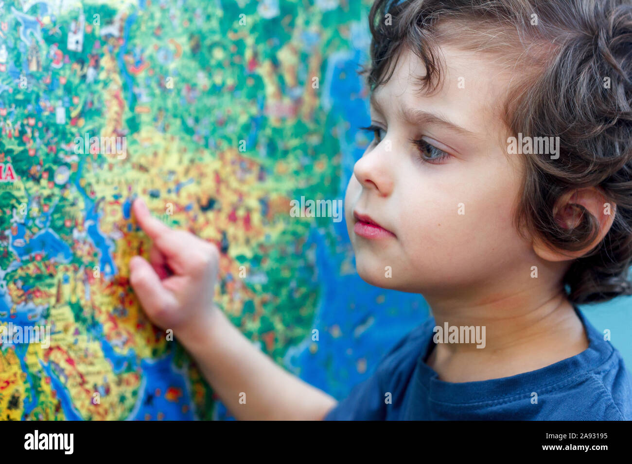 Das lockige Kind mit Interesse blickt auf die blaue Welt Karte Stockfoto