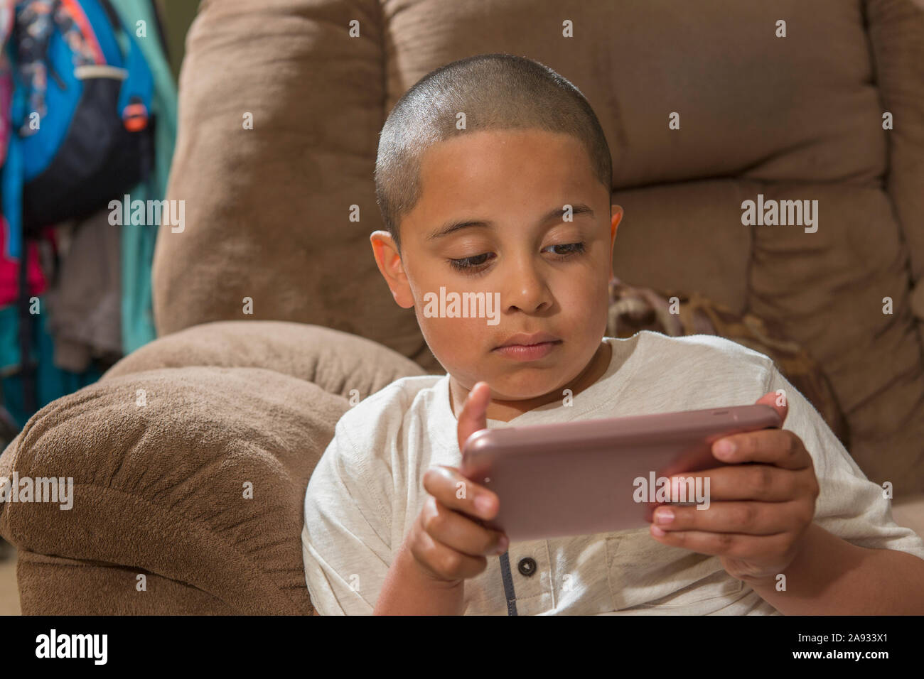 Hispanischer Junge mit Autismus, der ein elektronisches Spiel auf seinem spielt Telefon im Wohnzimmer Stockfoto