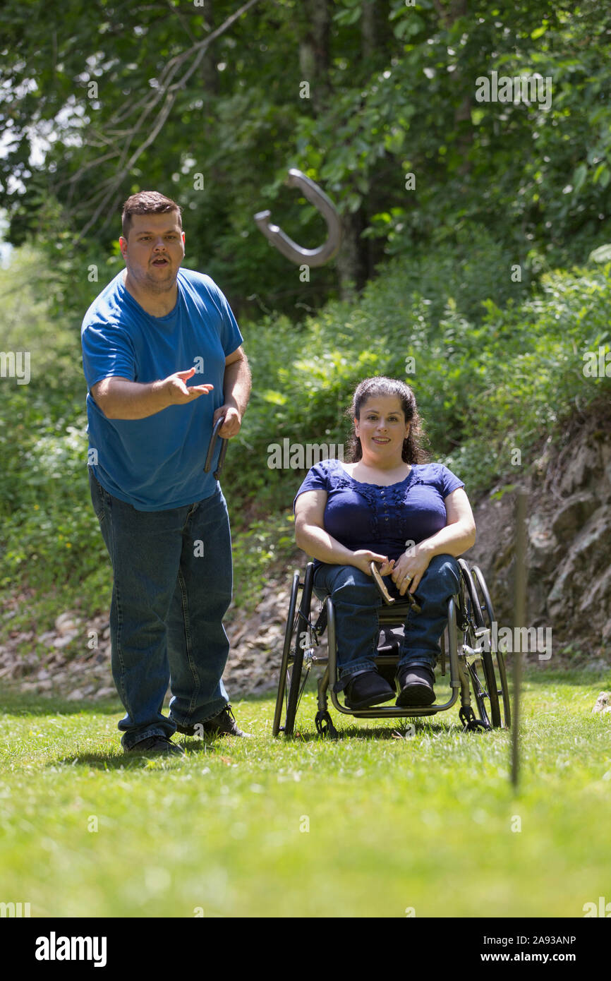 Frau mit Spina Bifida im Rollstuhl, die mit Hufeisen spielt Ihr Mann Stockfoto