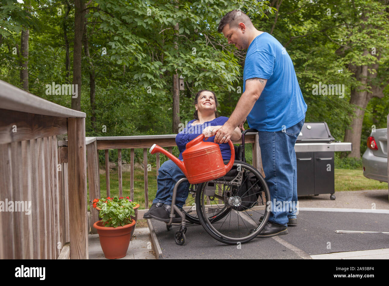 Frau mit Spina Bifida und ihr Mann wässern ihre Blumen Im Garten Stockfoto