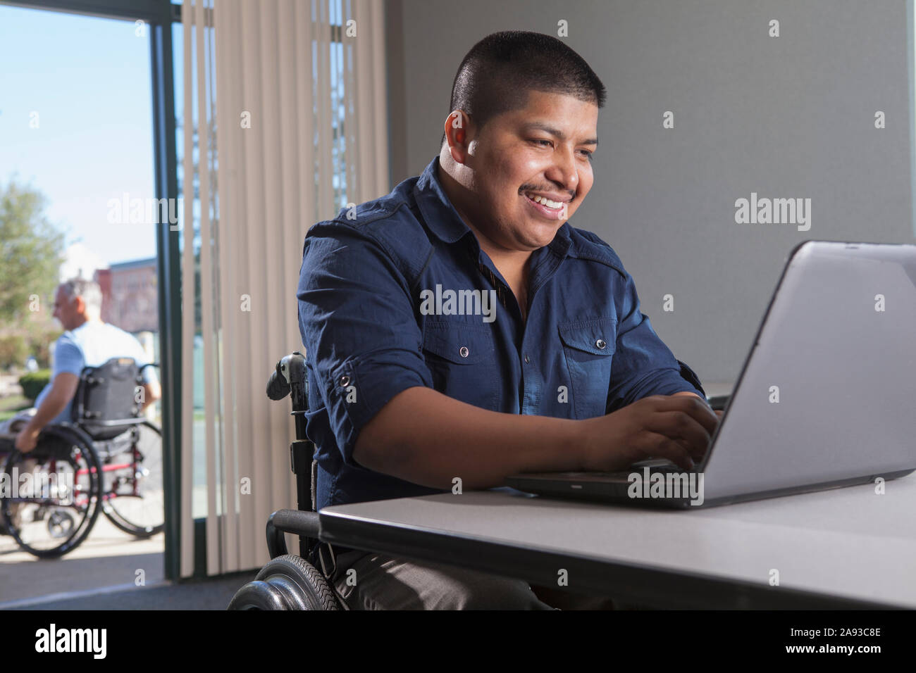 Hispanischer Mann im Rollstuhl mit Rückenmarksverletzung bei der Arbeit Stockfoto