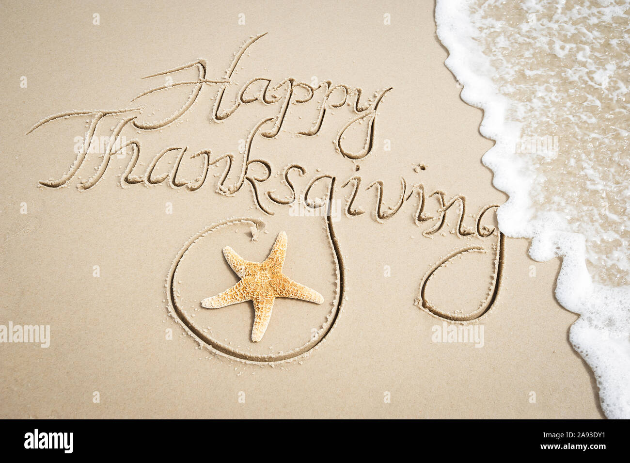 Happy Thanksgiving Nachricht handschriftlich auf glatten Sandstrand mit dekorativen Seesterne und entgegenkommende Welle Stockfoto
