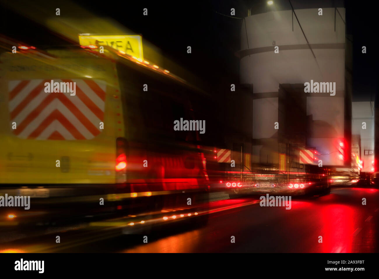 Begleitfahrzeug und übergroße Ladung Transport bei der Geschwindigkeit auf der Straße in einer regnerischen Nacht. Bild mit Filtern in der Postproduktion. Stockfoto