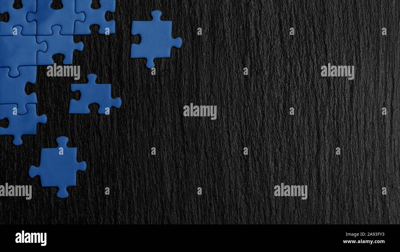 Blau Puzzle in der Ecke des Bildes auf einem schwarzen Hintergrund der Naturstein Schiefer. Ein Frame mit einem leeren Raum für ihre Beschreibung. Stockfoto