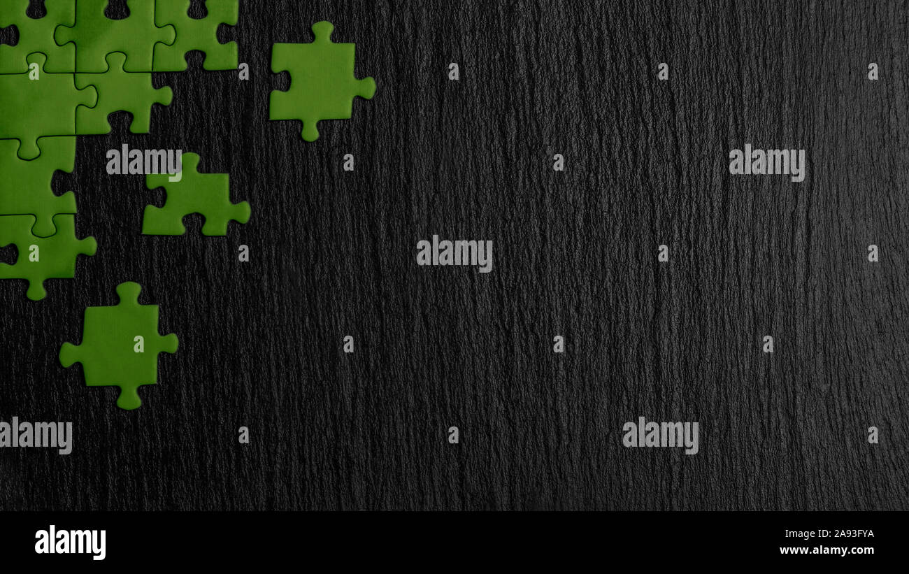 Grüne Puzzle in der Ecke des Bildes auf einem schwarzen Hintergrund der Naturstein Schiefer. Ein Frame mit einem leeren Raum für ihre Beschreibung. Stockfoto