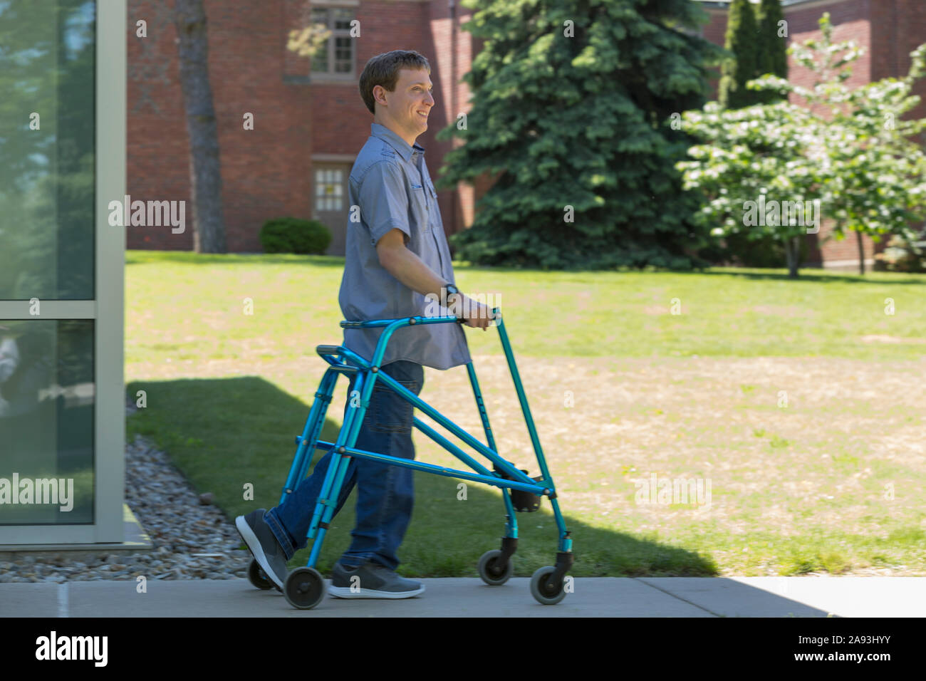 Junger Mann mit zerebraler Lähmung, der seinen Spaziergänger zum Gehen benutzt Zu arbeiten Stockfoto