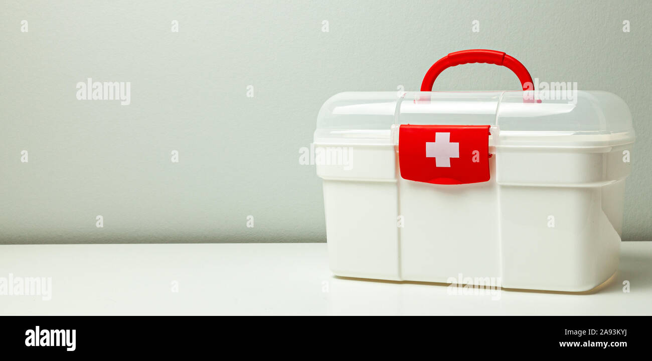Erste Hilfe Kit. Weißes Kästchen mit einem Kreuz und einer roten Verschluss auf grauem Hintergrund. Stockfoto