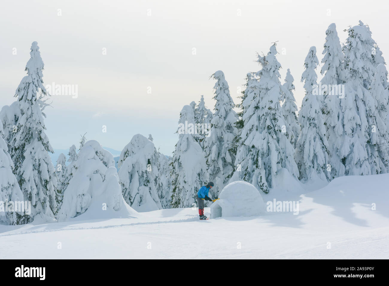 Mann in der blauen Jacke Gebäude Iglu in den hohen Bergen. Fantastische Winterlandschaft Stockfoto