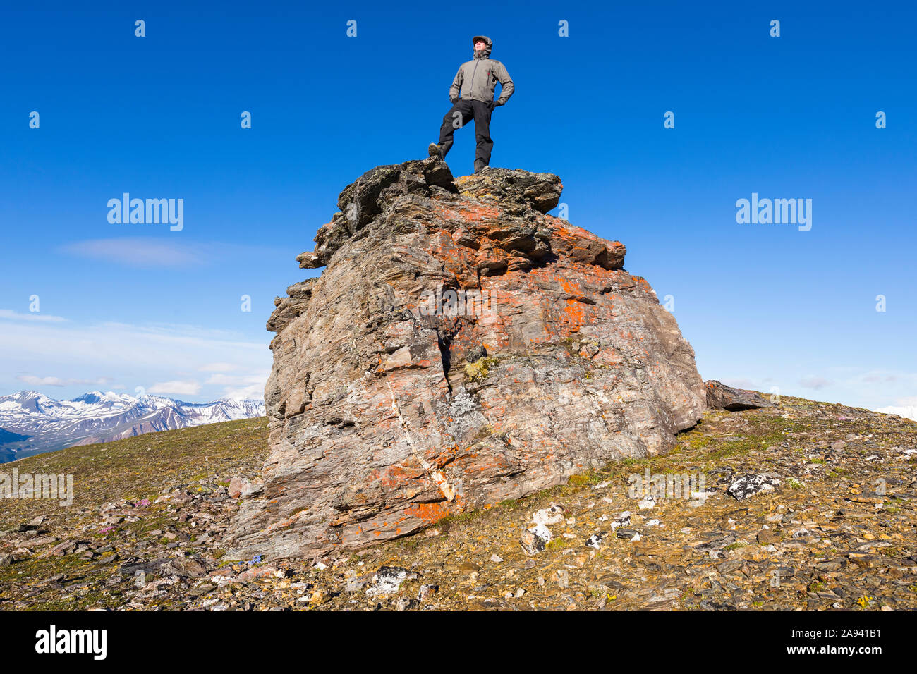 Ein Wanderer posiert auf einem Felsbrocken auf einem Bergrücken in der Alaska Range; Alaska, Vereinigte Staaten von Amerika Stockfoto