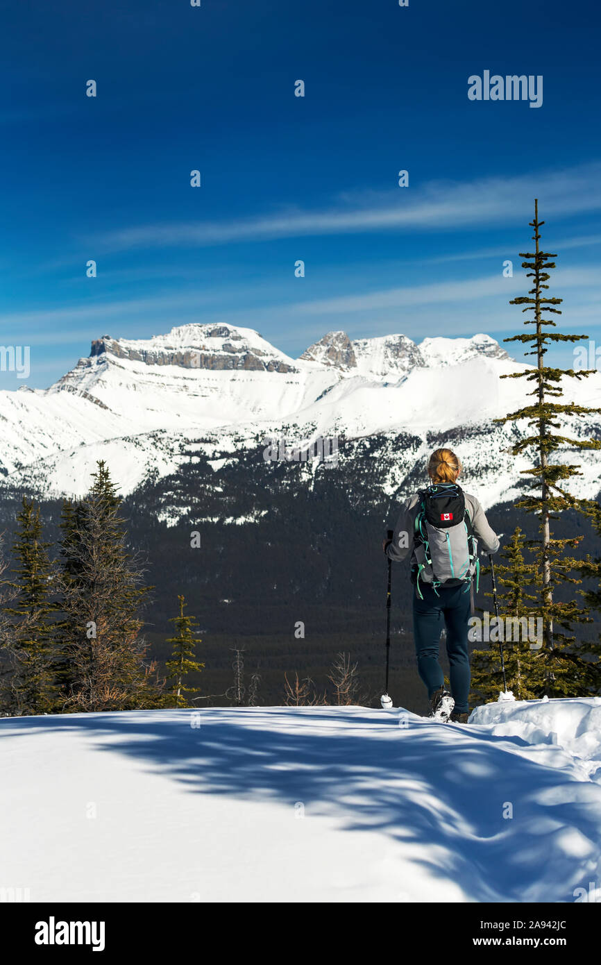 Weibliche Wanderer auf schneebedeckten Weg mit schneebedeckten Bergen, blauen Himmel und Wolken im Hintergrund; Lake Louise, Alberta, Kanada Stockfoto