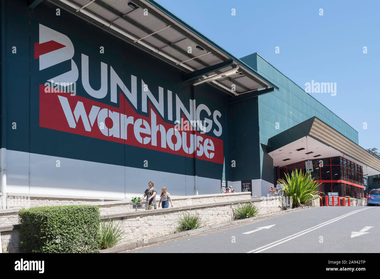 Die Menschen drücken Wagen hinter einem großen Bunnings Warehouse-Logo an der Seite eines Ihrer großen DIY-Verkaufsstellen im Sydney Vorort von belrose. Stockfoto