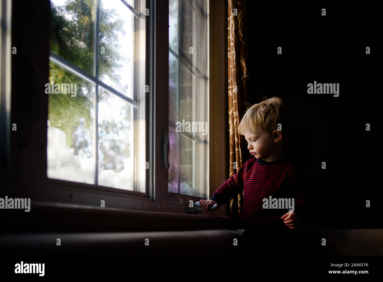 Ein kleiner Junge, der versucht, ein Fenster zu öffnen. Stockfoto
